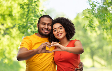 love, valentines day and people concept - happy african american couple making hand heart gesture over green natural background