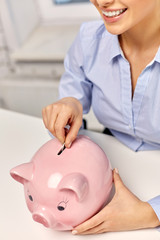 business, finances and investment concept - close up of happy smiling businesswoman with piggy bank and coin at office