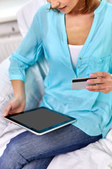 internet bank, online shopping and technology concept - happy young woman sitting on sofa with tablet pc computer and credit card at home
