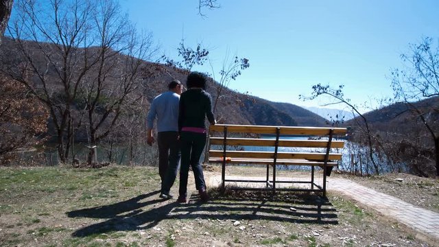 Rear view of a happy couple sitting together on bench outdoors near the lake and enjoying the view