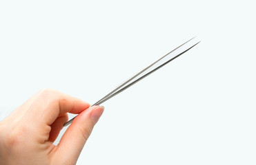 Metal medical tweezers with sharp edges in a woman's hand on a uniform background.