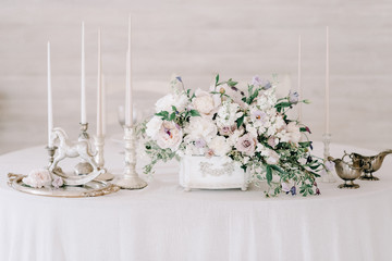 Wedding banquet table setting. Plates, glasses, cutlery and flower arrangement on a white round table. Round table with a white tablecloth. Plate with a gray cloth napkin.