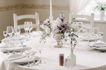 Wedding banquet table setting. Plates, glasses, cutlery and flower arrangement on a white round table. Round table with a white tablecloth. Plate with a gray cloth napkin.