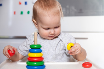 Adorable cute little baby is playing with colorful wooden pyramid