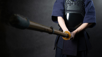 Kendo fighter in armor practicing with bamboo sword bokuto. Special bamboo sword and sports uniform. Photo of torso with hands.