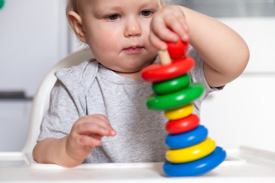 Adorable cute little baby is playing with colorful wooden pyramid