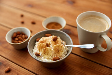 food and breakfast concept - oatmeal porridge in bowl with sliced banana, almond nuts and cinnamon and cup of coffee on wooden table