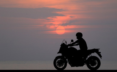 Obraz na płótnie Canvas Silhouette biker with his motorbike beside the natural lake and beautiful sunset sky.