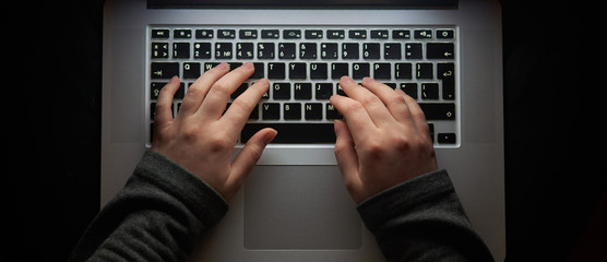 Overhead hacker in the hood working with laptop and mobile phone typing text in the darkroom....