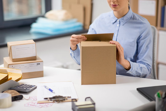 delivery, mail service, people and shipment concept - close up of woman packing parcel box at post office