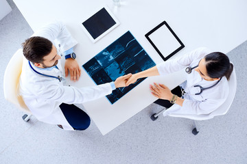 Medical team of doctors sitting and handshaking at table with tablets and x-ray, top view