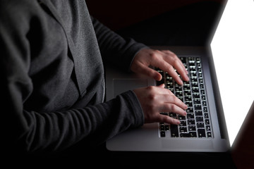 Overhead hacker in the hood working with laptop and mobile phone typing text in the darkroom. Russian hacker hacking the server in the dark. A hacker girl sitting in the dark with her laptop