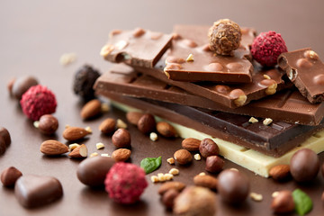 sweets, confectionery and food concept - close up of different chocolate bars, candies and nuts on brown background