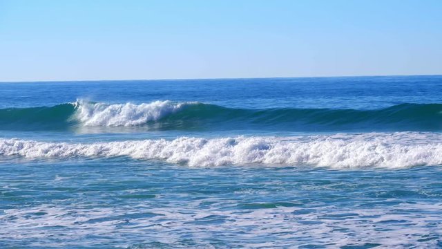 Waves surge consecutively against the seacoast under the blue sky in southern Portugal.