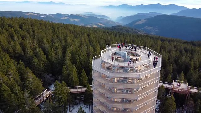 Drone zooming arc shot of Pohorje treetop path and the surrounding walkways where unrecognizable people enjoy the view