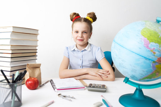 Back to school: Girl sitting at her desk and smiling. On the table are books, stationery and a globe.
