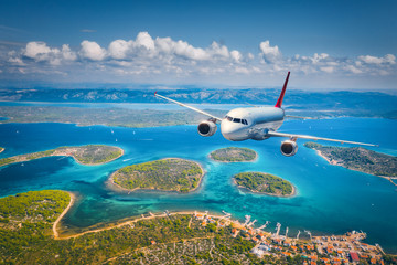 Airplane is flying over small islands and sea at sunny day in summer. Aerial view of passenger...