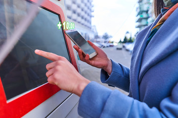 Person using street self service terminal and smartphone for pay for services. Digital technology...