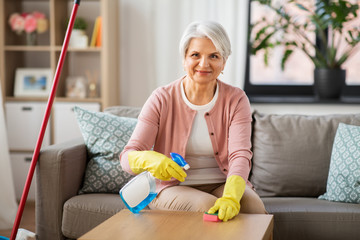 household and people concept - happy senior woman with detergent and sponge cleaning table at home