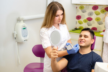 Young man sitting in chair at dental office and looking at mirror