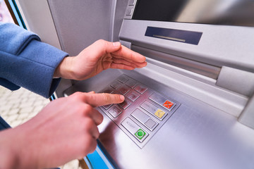 Person dials and hides with other hand for security purposes a PIN code on the keyboard of atm bank to withdraw money - obrazy, fototapety, plakaty