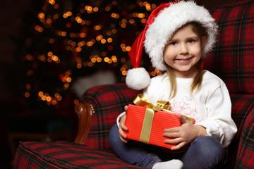 Fototapeta na wymiar Cute little child with Christmas gift sitting in armchair at home