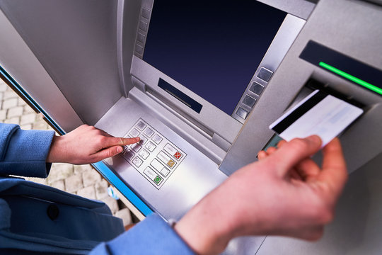 Person insert plastic credit card into atm machine and dials a PIN code on the keyboard to withdrawing cash