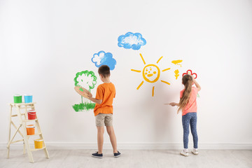 Little children painting on white wall indoors