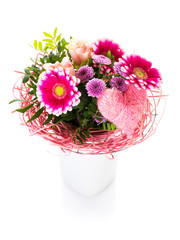 Bouquet with purple and pink flowers and heart-shaped ornament in a vase, isolated on white background