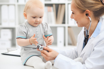 Doctor and patient in hospital. Little girl dressed in grey dress is being examined by doctor with stethoscope. Medicine concept