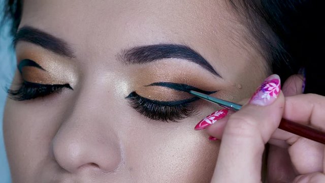 Beauty salon, makeup artist does evening makeup. Beautiful eyes with Golden eyeshadow. Eyebrow styling, Graphic bright arrows on the eyelids
