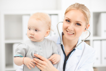 Doctor and patient in hospital. Little girl dressed in grey dress is being examined by doctor with stethoscope. Medicine concept