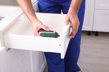 Worker installing kitchen furniture with electric screwdriver, closeup