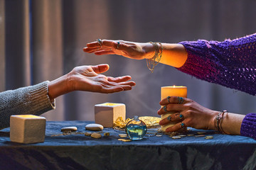 Gypsy witch woman during palmistry and divination ritual around candles and other magical...