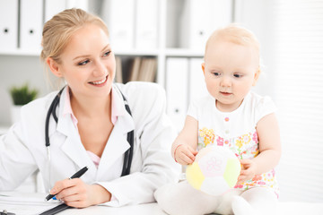 Doctor and patient toddler in hospital. Little girl dressed in dress with pink flowers is being examined by doctor with stethoscope. Medicine and health care concept