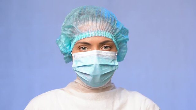 Female medical doctor in uniform, in a medical cap and a protective mask on her face looks seriously in the eyes, close-up. Looking at the camera. Medical Laboratory Researcher