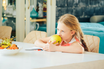 a little girl at the table with a notebook, doing homework and decided to eat a fresh Apple.