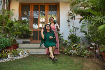 Women standing near a swing in the backyard and enjoying together. 