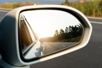 Mirror view of white car on the road heading towards the goal of the trip.