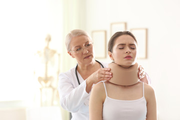 Fototapeta premium Female orthopedist applying cervical collar onto patient's neck in clinic