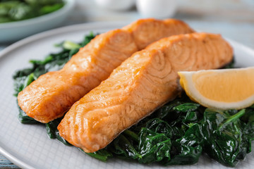 Tasty salmon with spinach and lemon on plate, closeup
