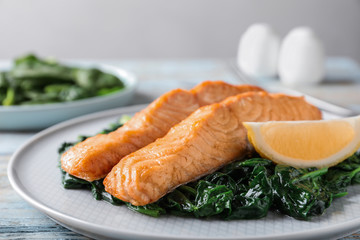 Tasty salmon with spinach and lemon on wooden table, closeup
