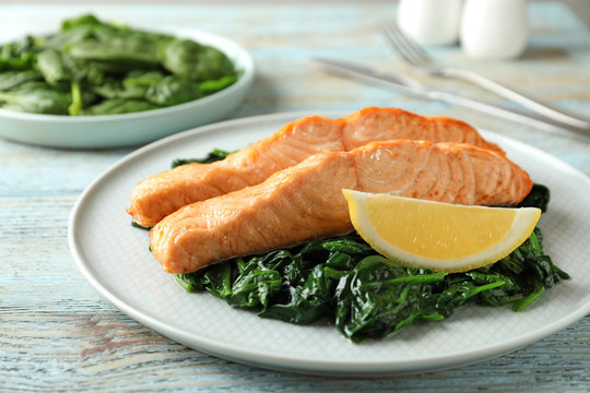 Tasty salmon with spinach and lemon on wooden table, closeup