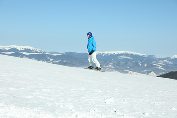 Male snowboarder on snowy slope in mountains. Winter vacation