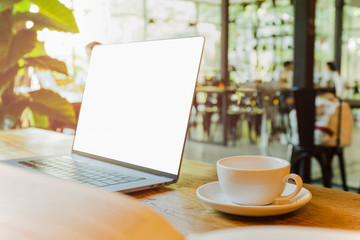 Selective focus on coffee cup and laptop on wooden table in blur background.