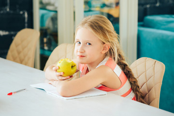 a little girl at the table with a notebook, decided to eat a fresh Apple