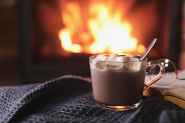 Delicious sweet cocoa with marshmallows and blurred fireplace on background