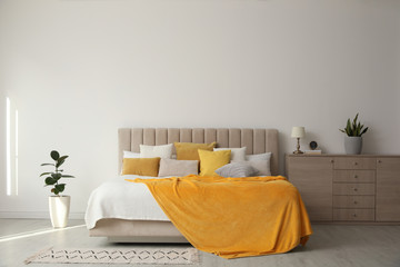Fototapeta na wymiar Stylish bedroom interior with soft yellow pillows and blanket