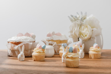 Selective focus of cupcakes with decorative bunnies, sugar bowl, easter cakes and vase with flowers isolated on grey