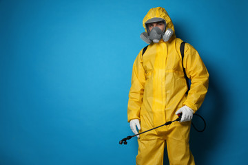 Man wearing protective suit with insecticide sprayer on blue background, space for text. Pest control - obrazy, fototapety, plakaty